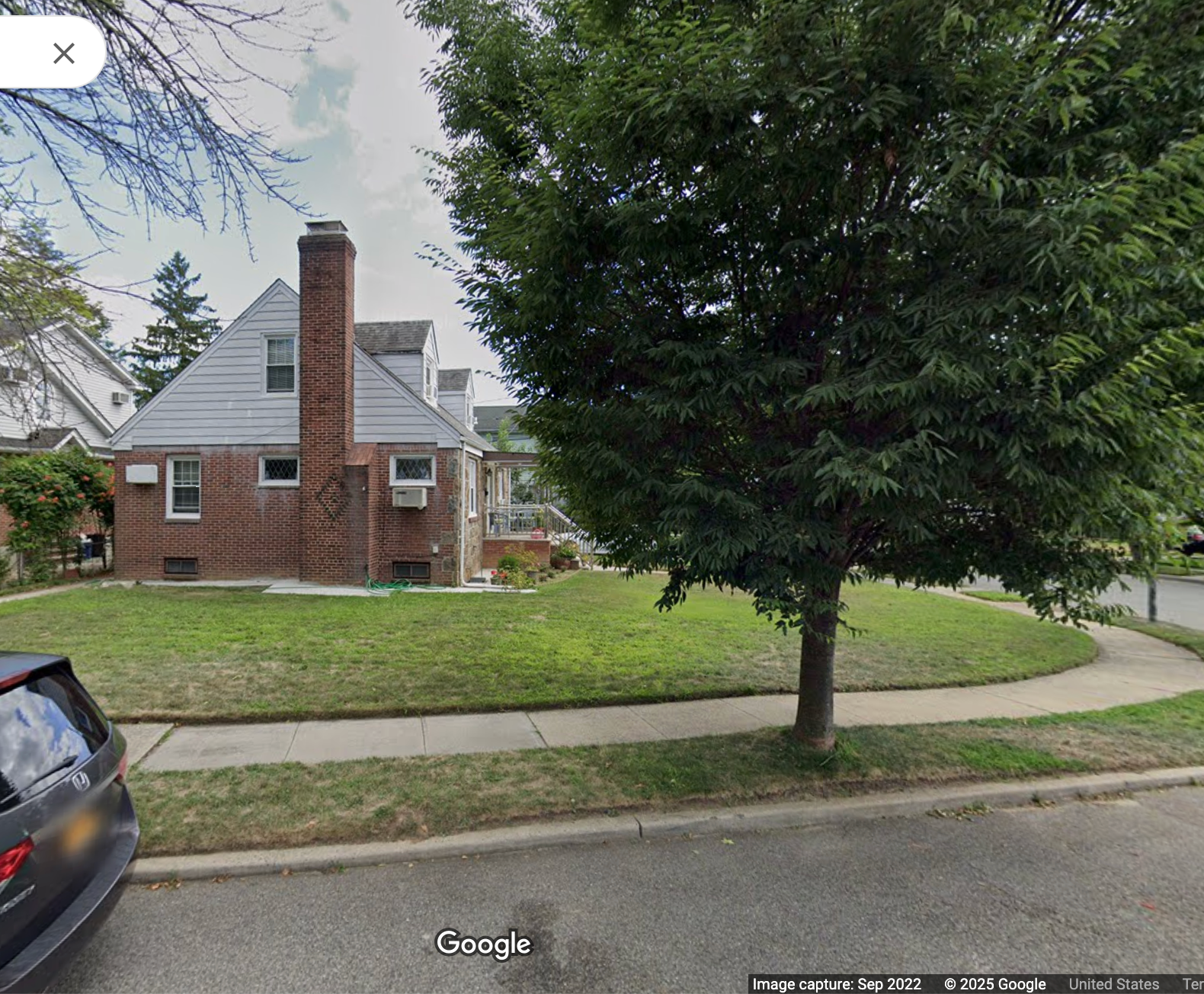 A suburban home with a plain, grassy lawn and a large tree on the periphery.